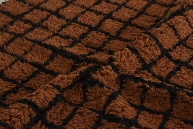 May include: Close-up of a brown, textured fabric with a repeating black grid pattern. The fabric has a soft, plush appearance, with a slightly uneven surface. The overall effect is warm and inviting.