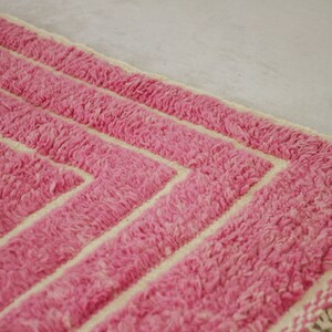 May include: Pink and cream striped rug with fringe on the edges. The rug has a geometric pattern.