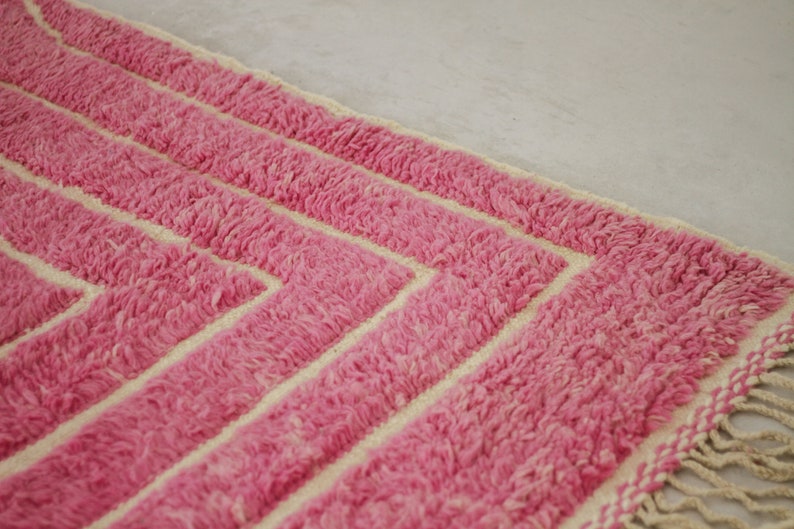 May include: Pink and cream striped rug with fringe on the edges. The rug has a geometric pattern.
