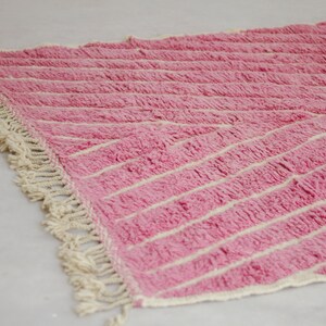 May include: Pink and white striped rug with a fringe border. The rug is made of a soft, fluffy material.