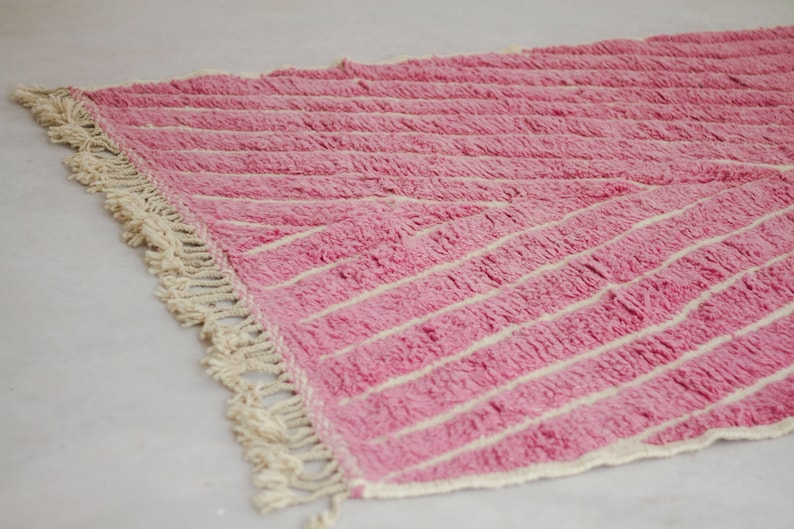 May include: Pink and white striped rug with a fringe border. The rug is made of a soft, fluffy material.