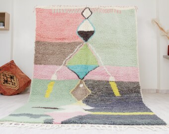 May include: A colorful Moroccan rug with a geometric pattern in shades of pink, green, blue, and gray. The rug has a fringe border and is made of wool.