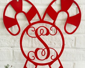 May include: Red metal candy cane Christmas ornament with a white brick background. The candy canes are joined at the top with a circle containing a monogrammed letter 'S'.