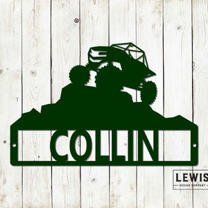 May include: Green metal silhouette of a buggy driving up a hill with the name "COLLIN" below. The silhouette is on a white wood background.