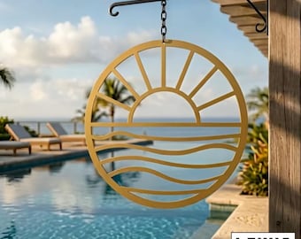 May include: A circular gold-colored metal wall sign featuring a cut-out design of a sun rising over wavy ocean water. The sign hangs from a black metal bracket by a short chain. The text "LEWIS DESIGN COMPANY" is visible in the bottom corner.