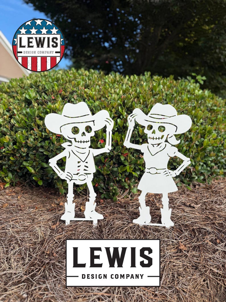 May include: Two white metal cowboy skeleton garden ornaments. One skeleton wears a vest and the other a dress. The ornaments are in front of a green bush. The text "LEWIS DESIGN COMPANY" is at the bottom.
