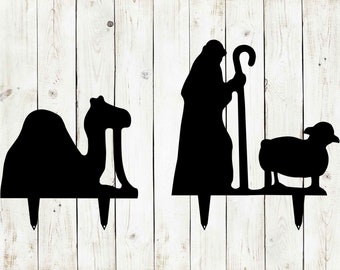 May include: Two black metal silhouette yard stakes. One features a camel and the other features a shepherd with a staff and a sheep.