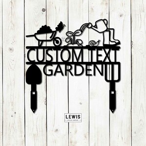 Puede incluir: Letrero de jard&iacute;n de metal negro con un dise&ntilde;o caprichoso que presenta a una persona regando plantas, una carretilla, una mariposa y un caracol. El letrero dice "CUSTOM TEXT GARDEN" con una pala y un rastrillo a cada lado.