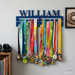 May include: A blue metal medal display with the name "WILLIAM" cut out at the top. The display holds numerous colorful ribbons and medals from various races and events. A baseball glove photo is in the background.