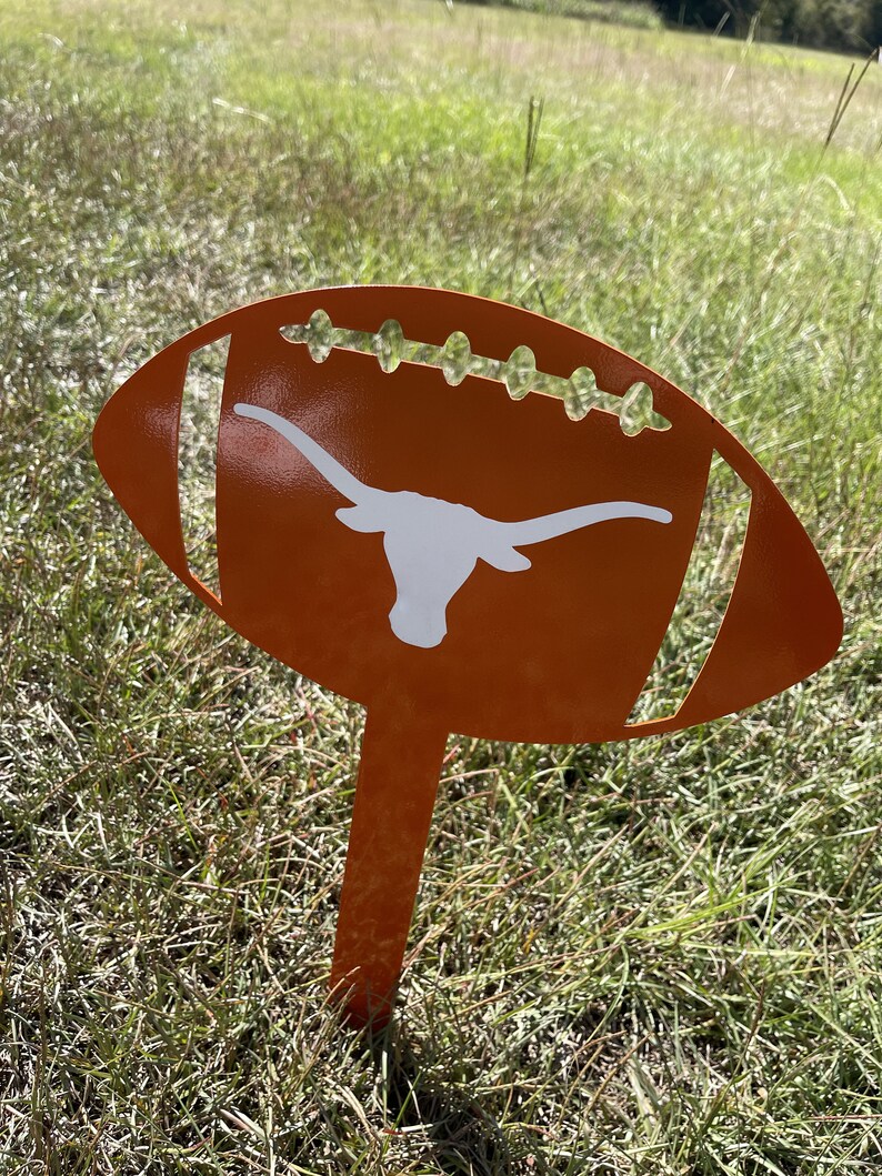 Peut inclure: Un piquet de jardin en m&eacute;tal orange en forme de ballon de football avec un logo de longhorn blanc. Le ballon de football pr&eacute;sente des d&eacute;tails d&eacute;coup&eacute;s et est plac&eacute; dans une zone herbeuse. Un objet d&eacute;coratif pour les fans de sport.