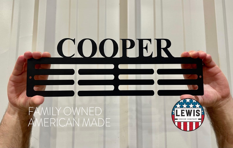 May include: Black metal sign with the name "COOPER" and three horizontal bars. The sign is held up by hands. The text "FAMILY OWNED AMERICAN MADE" is below the sign, and a circular logo is in the bottom right corner.
