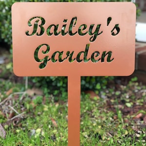 May include: A copper-colored metal garden sign with the text "Bailey's Garden" cut out in a decorative font.