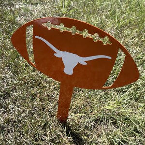 Peut inclure: Un piquet de jardin en m&eacute;tal orange en forme de ballon de football avec un logo de longhorn blanc. La d&eacute;coration en forme de ballon de football pr&eacute;sente des d&eacute;tails d&eacute;coup&eacute;s et est plac&eacute;e dans une zone herbeuse. Un article d&eacute;coratif pour les fans de sport.