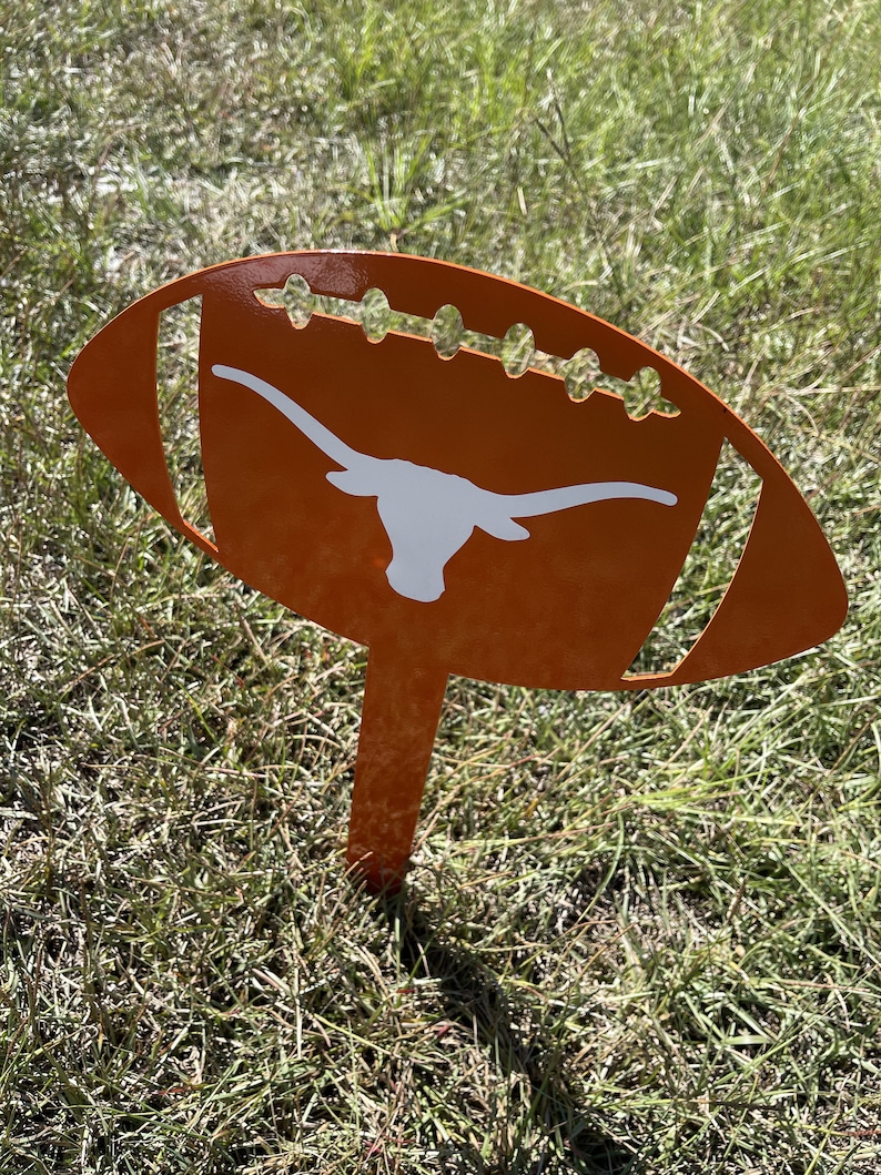 Peut inclure: Un piquet de jardin en m&eacute;tal orange en forme de ballon de football avec un logo de longhorn blanc. La d&eacute;coration en forme de ballon de football pr&eacute;sente des d&eacute;tails d&eacute;coup&eacute;s et est plac&eacute;e dans une zone herbeuse. Un article d&eacute;coratif pour les fans de sport.