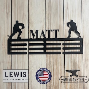 May include: Black metal hockey medal display with the name "MATT" and two hockey players silhouettes. The display has five rows of hooks for medals. The display is made in the USA.