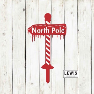 May include: Red metal sign with a candy cane pole and the words "North Pole" on a white wooden background. The sign has icicles hanging from the bottom.