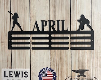 May include: Black metal medal display rack with a baseball player silhouette on each end. The rack has 10 slots for medals and the name "APRIL" is in the center. The rack is made in the USA.