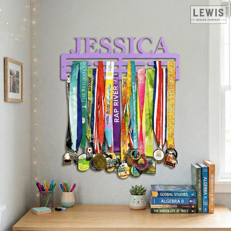 May include: A lavender-colored medal display with the name "JESSICA" cut out at the top. Colorful ribbons and medals hang from the display. The display is mounted on a gray wall above a wooden desk.