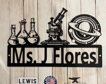 May include: Black metal sign with the text "Ms. J Flores" and a design of a microscope, beakers, and a planet with rings.