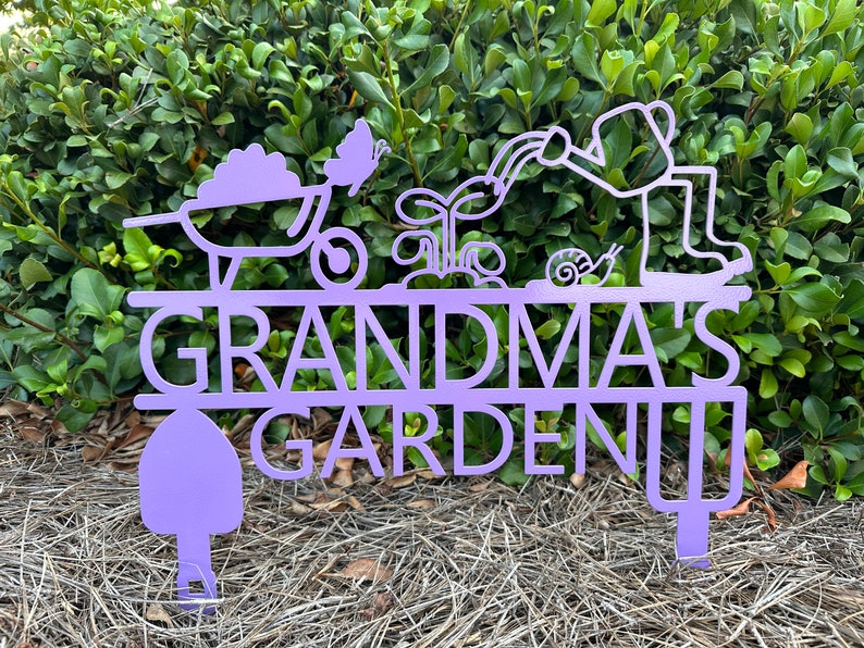 Puede incluir: Se&ntilde;al de jard&iacute;n de metal morado con el texto "Grandma's Garden" y una carretilla, una mariposa, una planta, un caracol y una persona regando una planta.