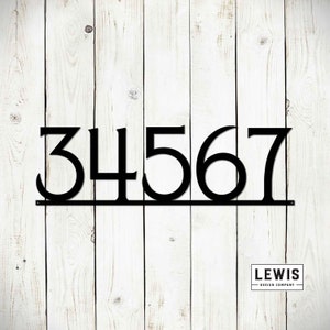 May include: Black metal house numbers 34567 with a horizontal bar underneath. The numbers are attached to a white wooden surface. The text "LEWIS DESIGN COMPANY" is visible in the bottom right corner.