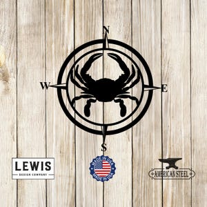 May include: Black metal compass with a crab silhouette in the center. The compass points are labeled N, S, E, and W. The compass is on a wood background with a "Made in USA" label and "American Steel" text.