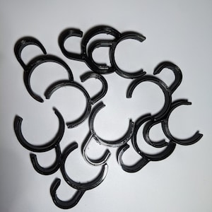 Op de afbeelding: Een stapel zwarte plastic haken. De haken zijn allemaal even groot en even gevormd, en ze zijn in een willekeurig patroon gerangschikt.