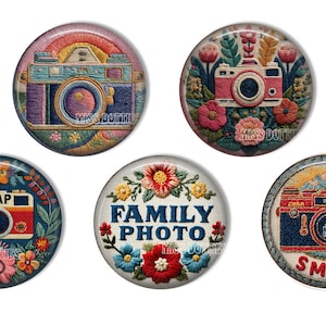 May include: Five circular pins featuring embroidered camera and floral designs. One pin shows a blue camera, one a pink camera with flowers, one a red camera with the word SNAP, one with the text FAMILY PHOTO, and one a red camera with the word SMILE.
