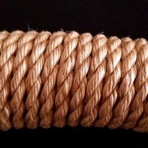 May include: Close-up of a thick, natural-fibre rope with a light brown colour. The rope is tightly woven and has a textured surface.