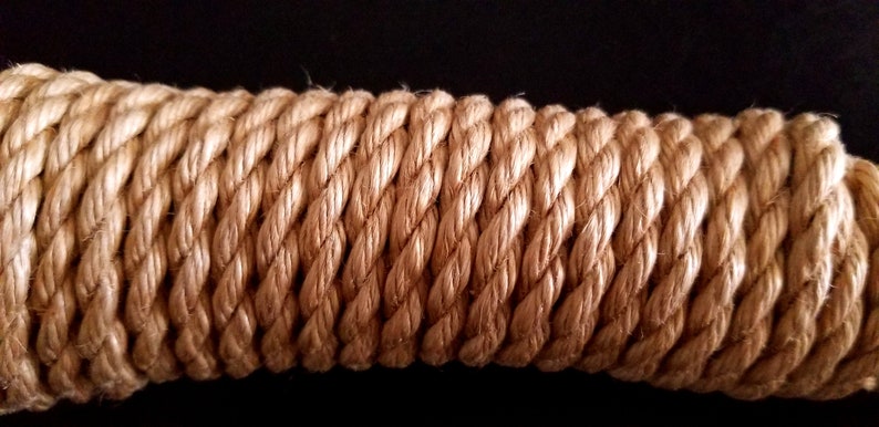 May include: Close-up of a thick, natural-fibre rope with a light brown colour. The rope is tightly woven and has a textured surface.