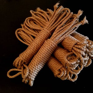 May include: A bundle of brown natural fibre rope, likely sisal or hemp, is arranged in a loose pile. The rope is thick and textured, with a natural, rustic look.