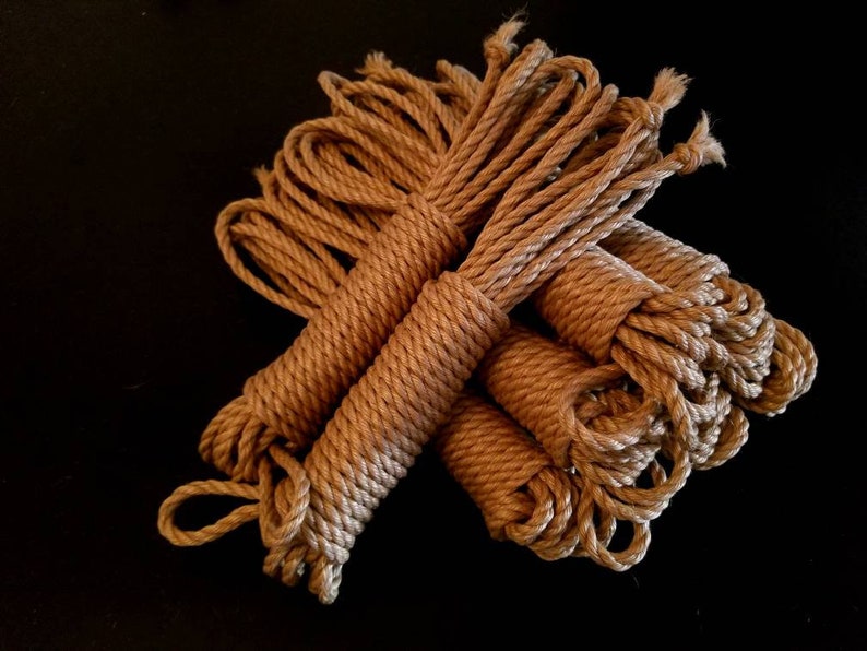 May include: A bundle of brown natural fibre rope, likely sisal or hemp, is arranged in a loose pile. The rope is thick and textured, with a natural, rustic look.