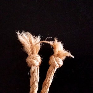 May include: Two beige rope ends tied together in a knot. The rope is frayed at the ends.