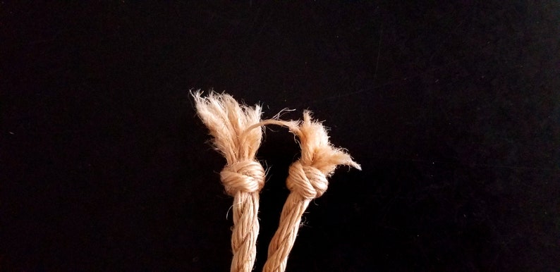 May include: Two beige rope ends tied together in a knot. The rope is frayed at the ends.