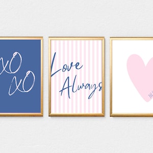 May include: Three framed art prints with gold frames. The left print is blue with white "xo xo" text. The center print has pink and white stripes with "Love Always" text. The right print has a pink heart with "I'll be here" text.
