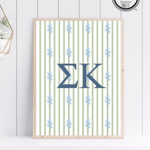 May include: Framed wall art featuring a light green and white striped background with blue floral accents. The Greek letters ΣΚ are centered in navy blue. The artwork is in a light wood frame and includes an "Affinity Licensed Product" seal.
