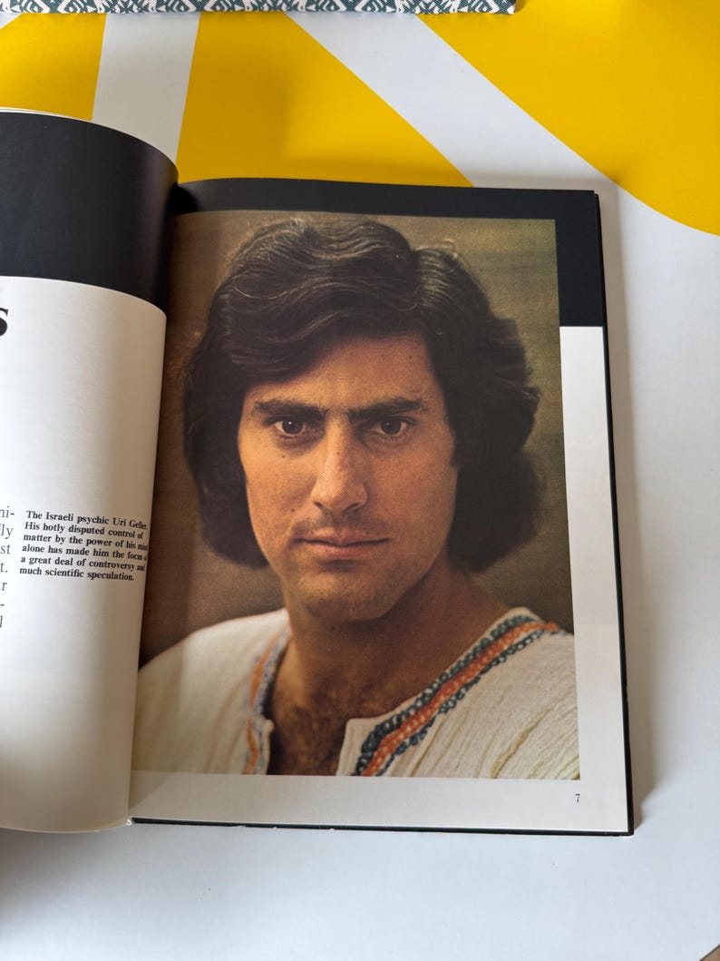 May include: A portrait of a man with dark hair and a white shirt with orange and blue trim. The image is from a book, with text visible on the left page. The man is looking directly at the viewer.