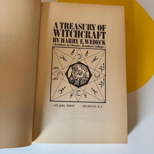 May include: Open book with the title "A Treasury of Witchcraft" by Harry E. Wedeck. The cover features a black and white illustration of a geometric design with symbols and a central figure. Published by Citadel Press.