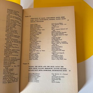 May include: Open book with text about magic, spells, and rituals. The pages are yellowed, and the text is in black. Chapters III and IV are visible, with titles like "Operations of Magic" and "Raising the Devil."