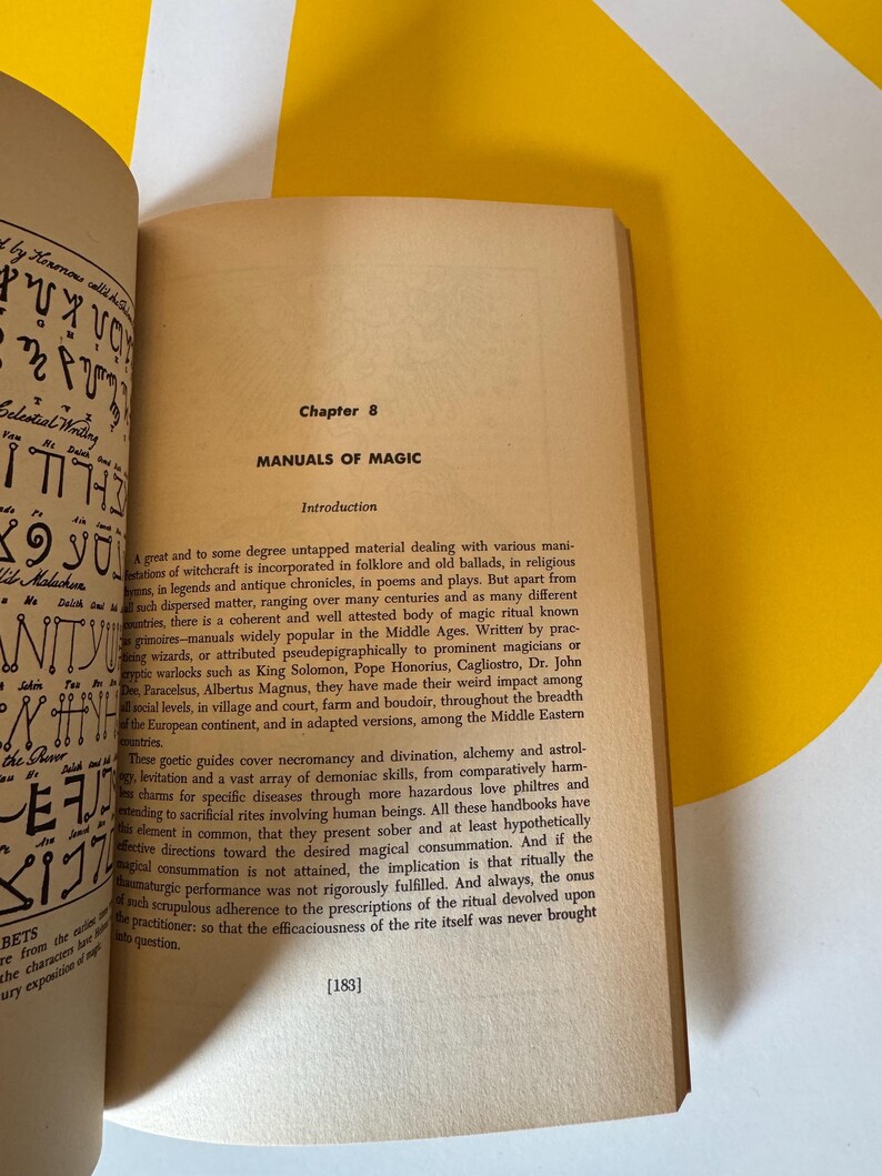 May include: An open book with text on aged paper, featuring the title "MANUALS OF MAGIC" under Chapter 8. The book's pages are cream-colored, with black text. The background includes a yellow and white angled surface.