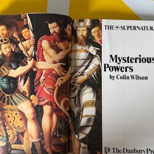 May include: Open book with a colorful illustration of several figures in ancient attire. The text on the right page reads "Mysterious Powers by Colin Wilson" under "THE SUPERNATURAL". Published by The Danbury Press.