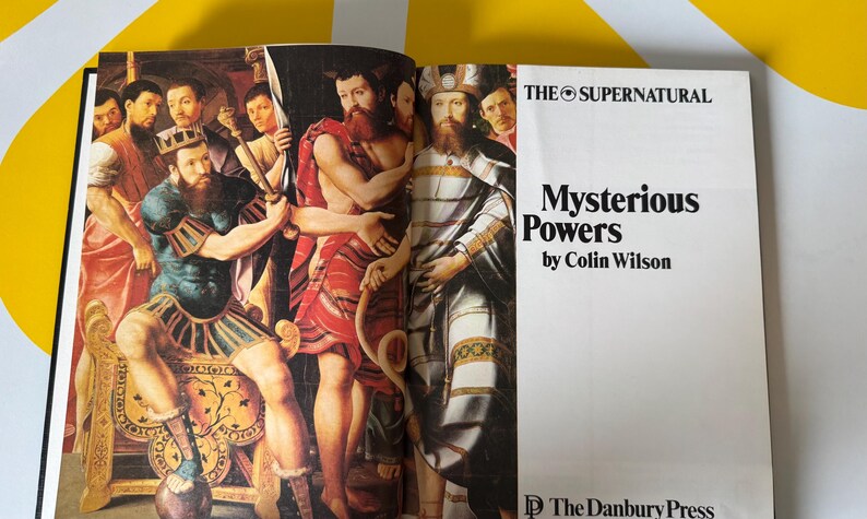 May include: Open book with a colorful illustration of several figures in ancient attire. The text on the right page reads "Mysterious Powers by Colin Wilson" under "THE SUPERNATURAL". Published by The Danbury Press.