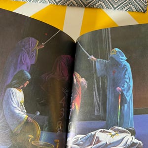 May include: An illustration from a book depicting figures in hooded robes, some holding swords. The figures are in shades of blue, purple, and white. One figure is standing over a person lying on the ground.