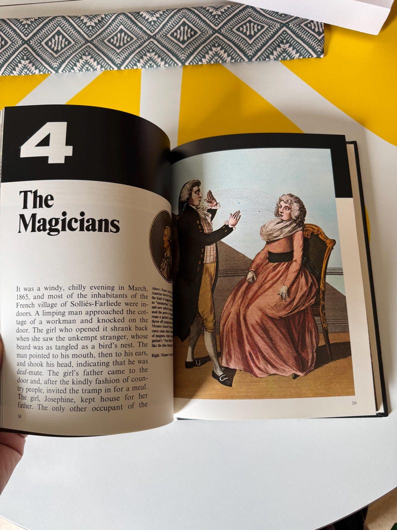 May include: Open book with the title "The Magicians" and a vintage illustration of two people in period clothing. The illustration depicts a man gesturing and a woman seated in a chair. The page numbers are visible.