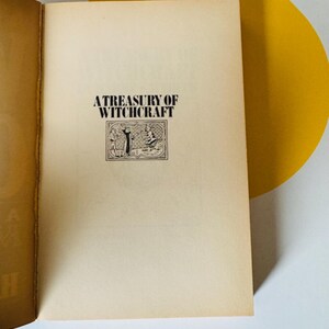 May include: Open book with the title "A Treasury of Witchcraft" printed in black on a cream-colored page. The title is above a small illustration of two figures. The book's pages have a vintage, aged appearance.