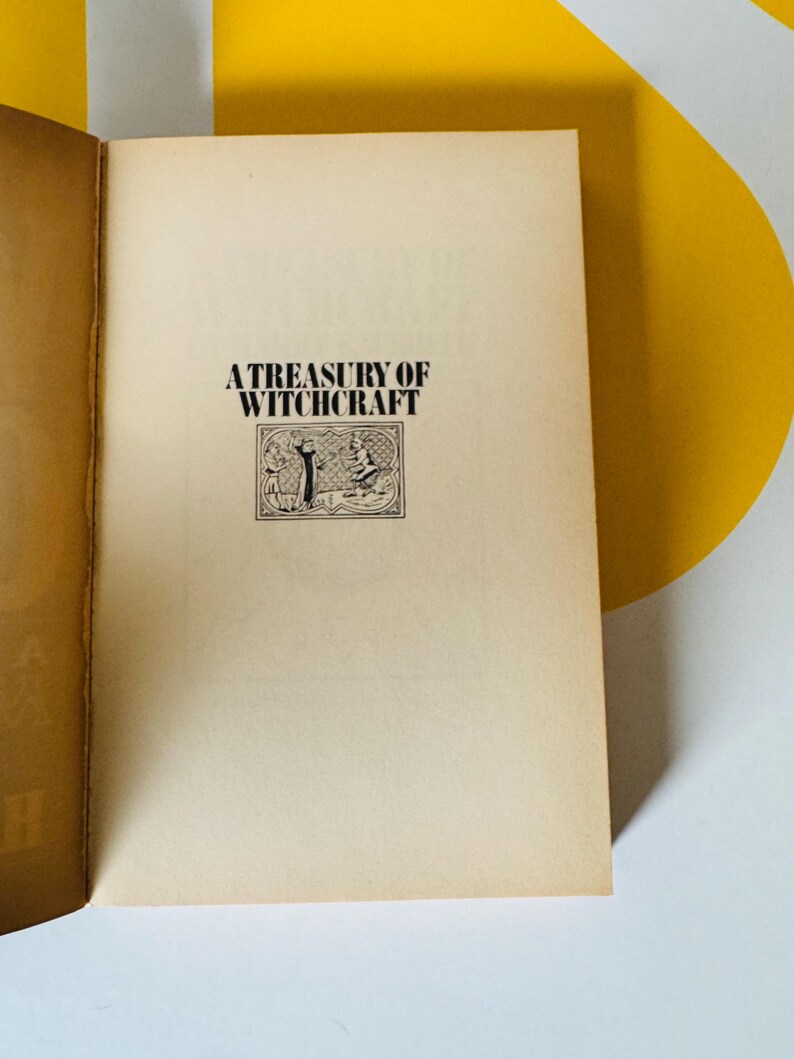 May include: Open book with the title "A Treasury of Witchcraft" printed in black on a cream-colored page. The title is above a small illustration of two figures. The book's pages have a vintage, aged appearance.