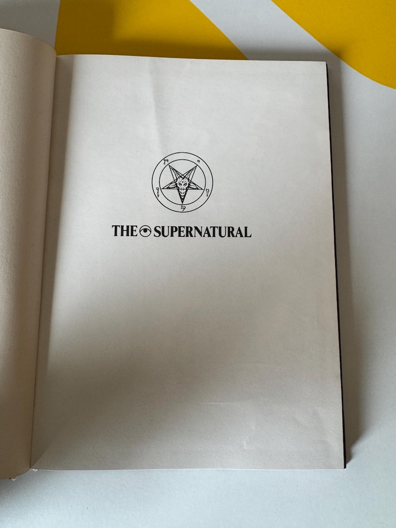 May include: Open book with the title "THE SUPERNATURAL" printed in black. Above the title is a circular emblem with a five-pointed star inside a circle. The book's pages are off-white.