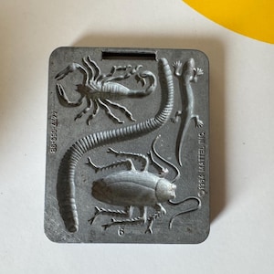 May include: A vintage gray insect mold featuring a scorpion, worm, lizard, and beetle. The mold is rectangular with a handle and the text "©1984 MATTEL INC." and "35-650-4477".