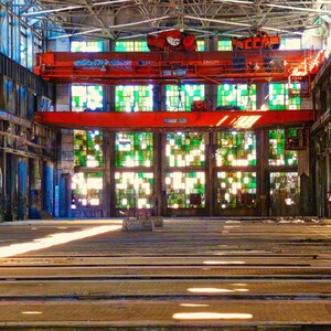 May include: An interior shot of a large industrial building with a high ceiling and a red overhead crane. The building has large windows with stained glass, and the floor is made of wooden planks. The overall color scheme is a mix of blue, green, and brown.
