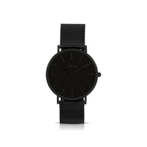 May include: A minimalist black wristwatch with a mesh band. The watch face is round and black, with simple black hour markers and hands. The brand name "Vance" is printed in the center. The watch has a sleek, modern design.